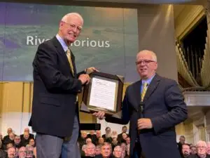 Steve Pace, president of Alabama Singing Men, presents Tom Smith with a framed copy of River Glorious, a choral anthem commissioned for him to celebrate his 25 years of service as he retires as ASM conductor.